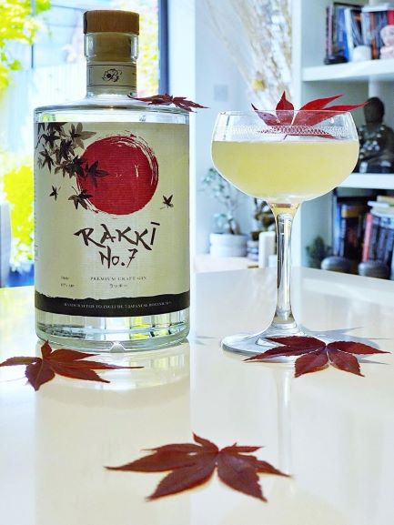 a bottle of rakki gin on a table with a cocktail and a garden in the background