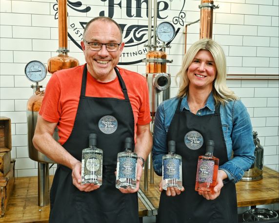 a man and a woman in a distillery setting holding bottles of gin