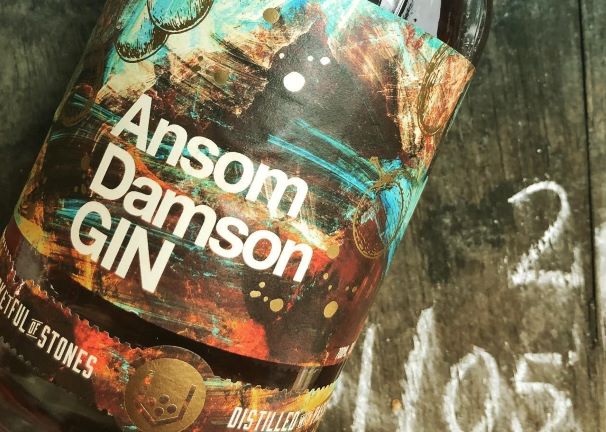 A BOTTLE OF ANSOM DAMSON GIN ON A WOODEN TABLE WITH CHALK WRITING