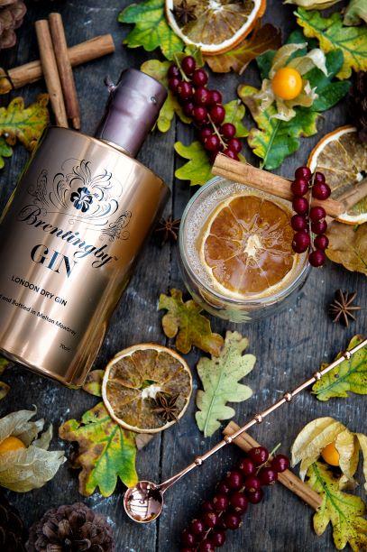 a bottle of brentingby london dry gin with leaves and citrus on a wooden table with a cocktail