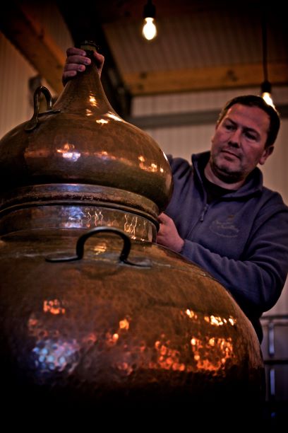 a man working on a copper still in a distillery