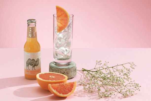 a bottle of two keys pink grapefruit with a paloma cocktail on a table with a pink background