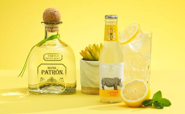 a tequila cocktail with a bottle of two keys lemon mixer on a yellow background