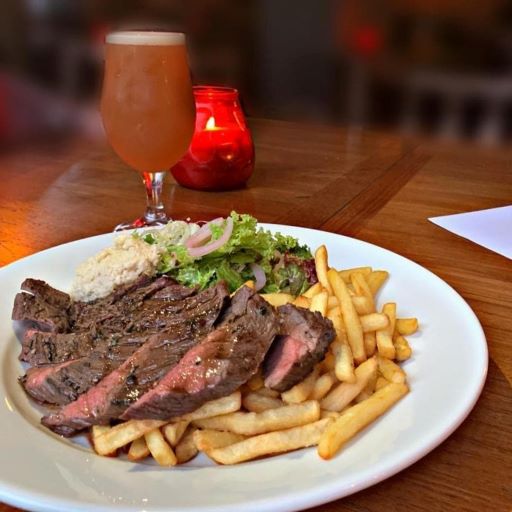a plate of steak and chips with a beer in the background